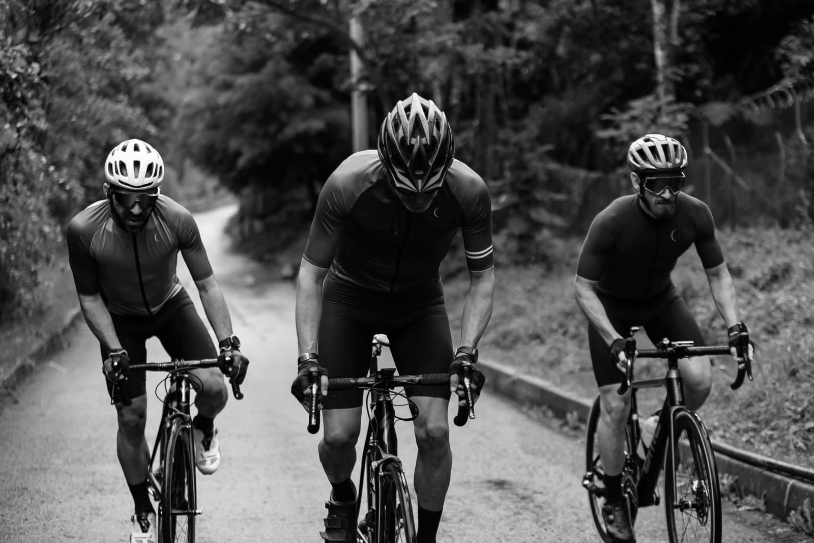 Trois cyclistes roulant en ligne sur une route étroite bordée d'arbres